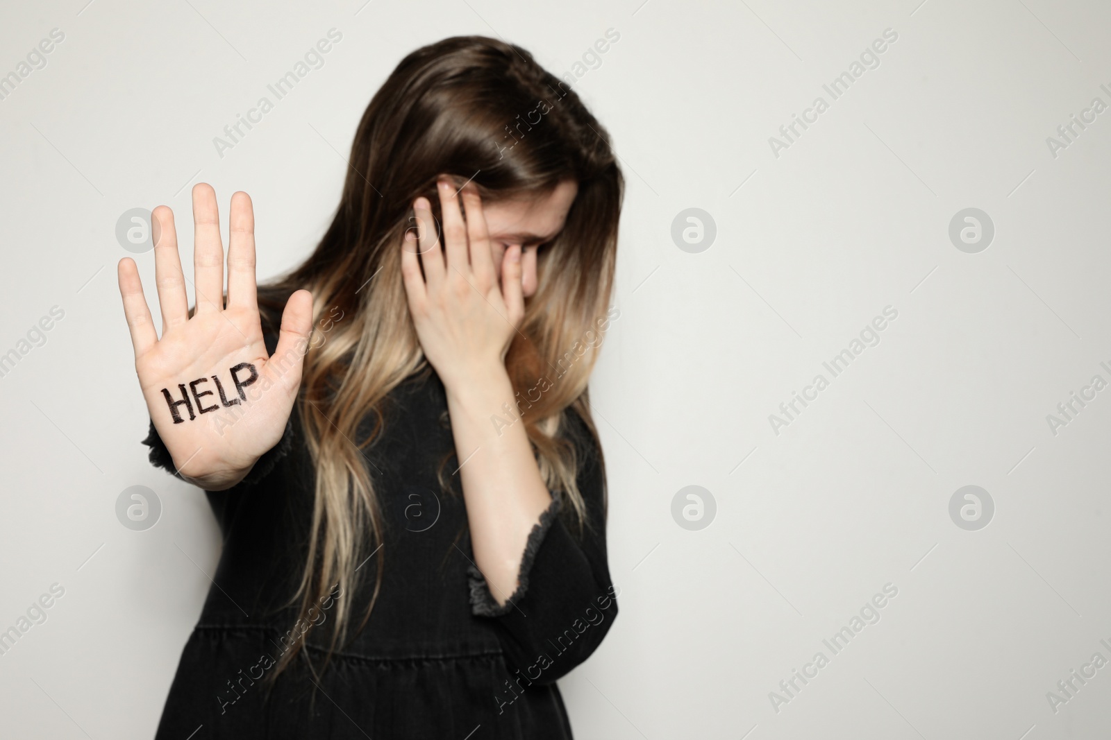 Photo of Young woman with word HELP written on her palm against light background, focus on hand. Space for text