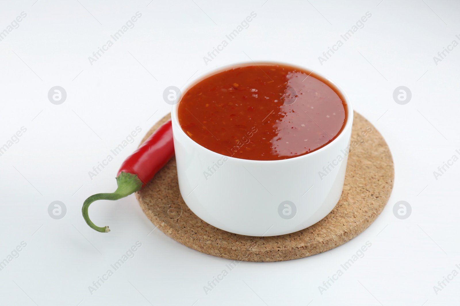 Photo of Spicy chili sauce in bowl and fresh pepper on white background