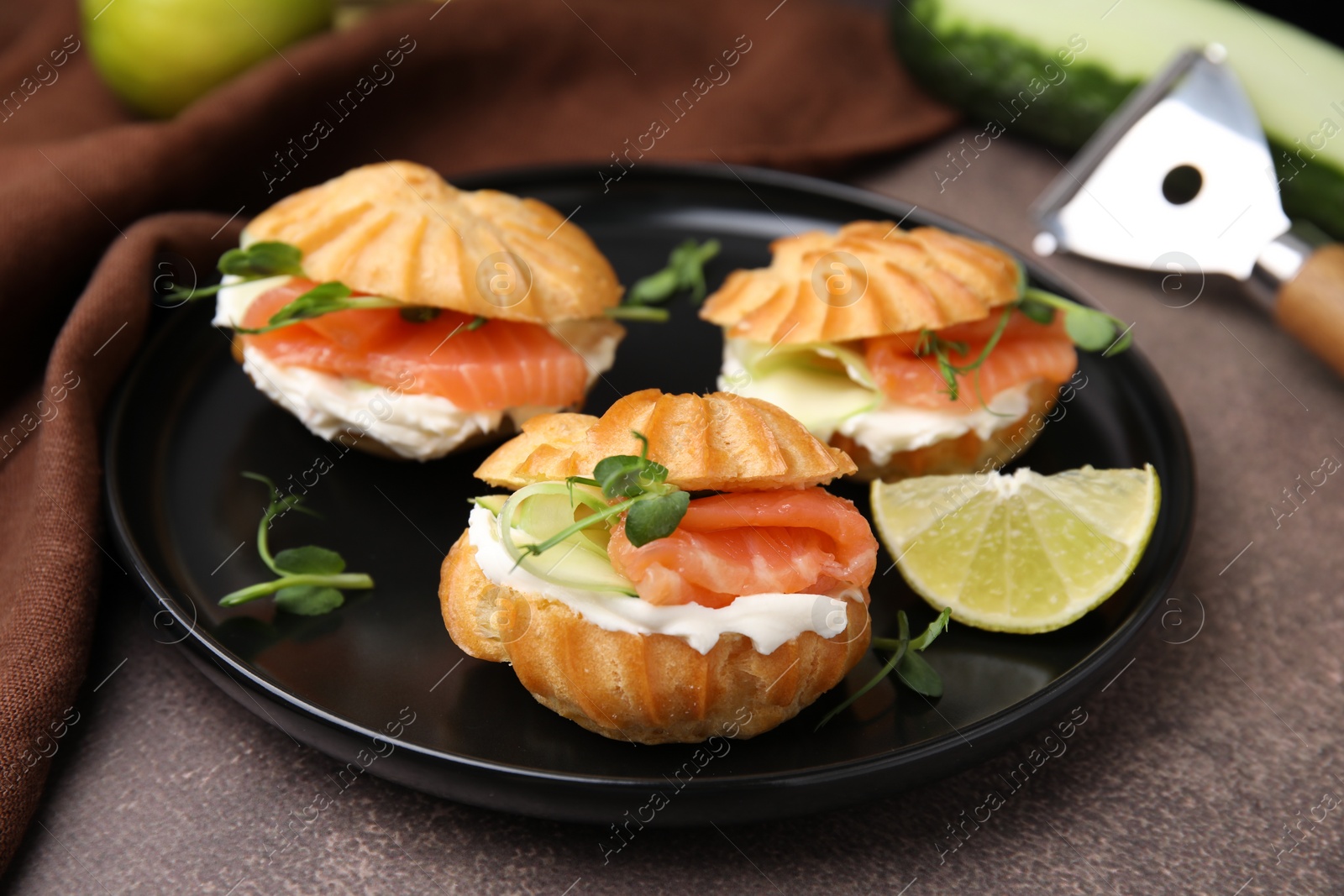 Photo of Delicious profiteroles with cream cheese, salmon and cucumber on textured table, closeup