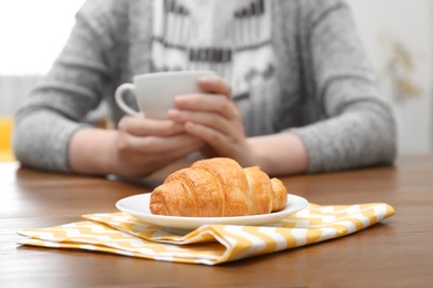 Photo of Young woman having breakfast with tasty croissant and cup of coffee at table