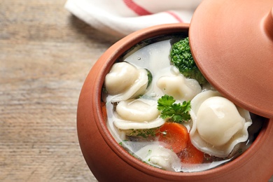 Photo of Pot of tasty dumplings with broth and vegetables on wooden table, closeup. Space for text