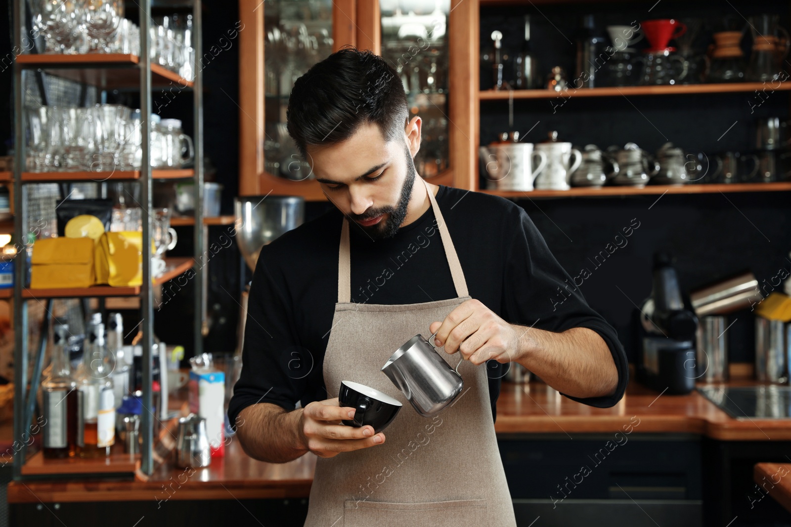 Photo of Portrait of barista pouring milk into cup of coffee against bar shelves in cafe