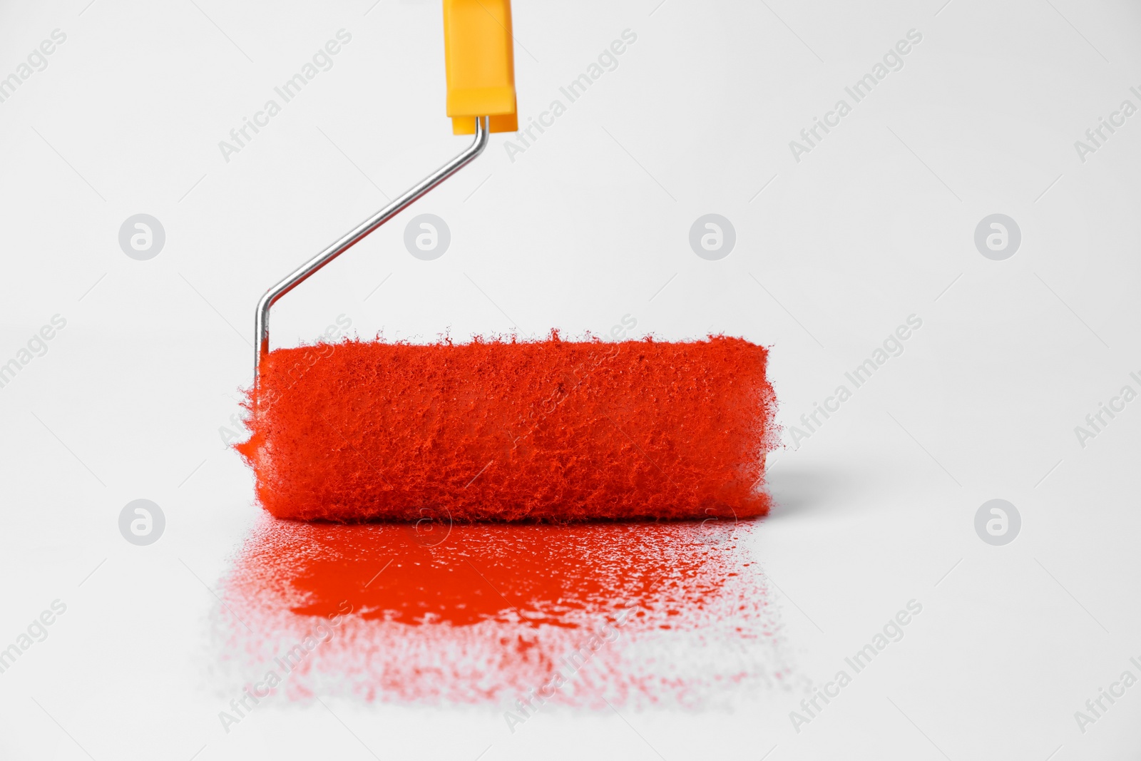 Photo of Roller brush and strokes of orange paint on white background