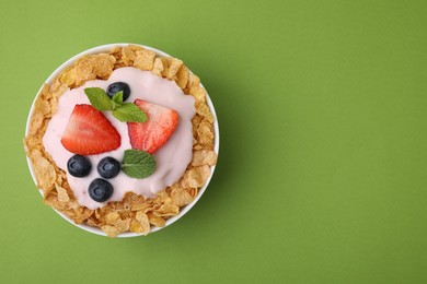 Photo of Delicious crispy cornflakes, yogurt and fresh berries in bowl on green background, top view with space for text. Healthy breakfast