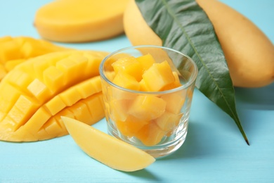 Photo of Fresh mango cubes in glass and juicy fruit on table, closeup