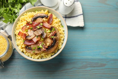 Tasty millet porridge with mushrooms, bacon and green onion in bowl on light blue wooden table, flat lay. Space for text