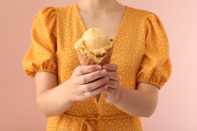 Photo of Woman holding yellow ice cream in wafer cone on pink background, closeup