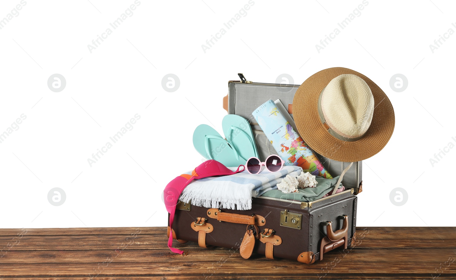 Photo of Open vintage suitcase with different beach objects packed for summer vacation on wooden table against white background