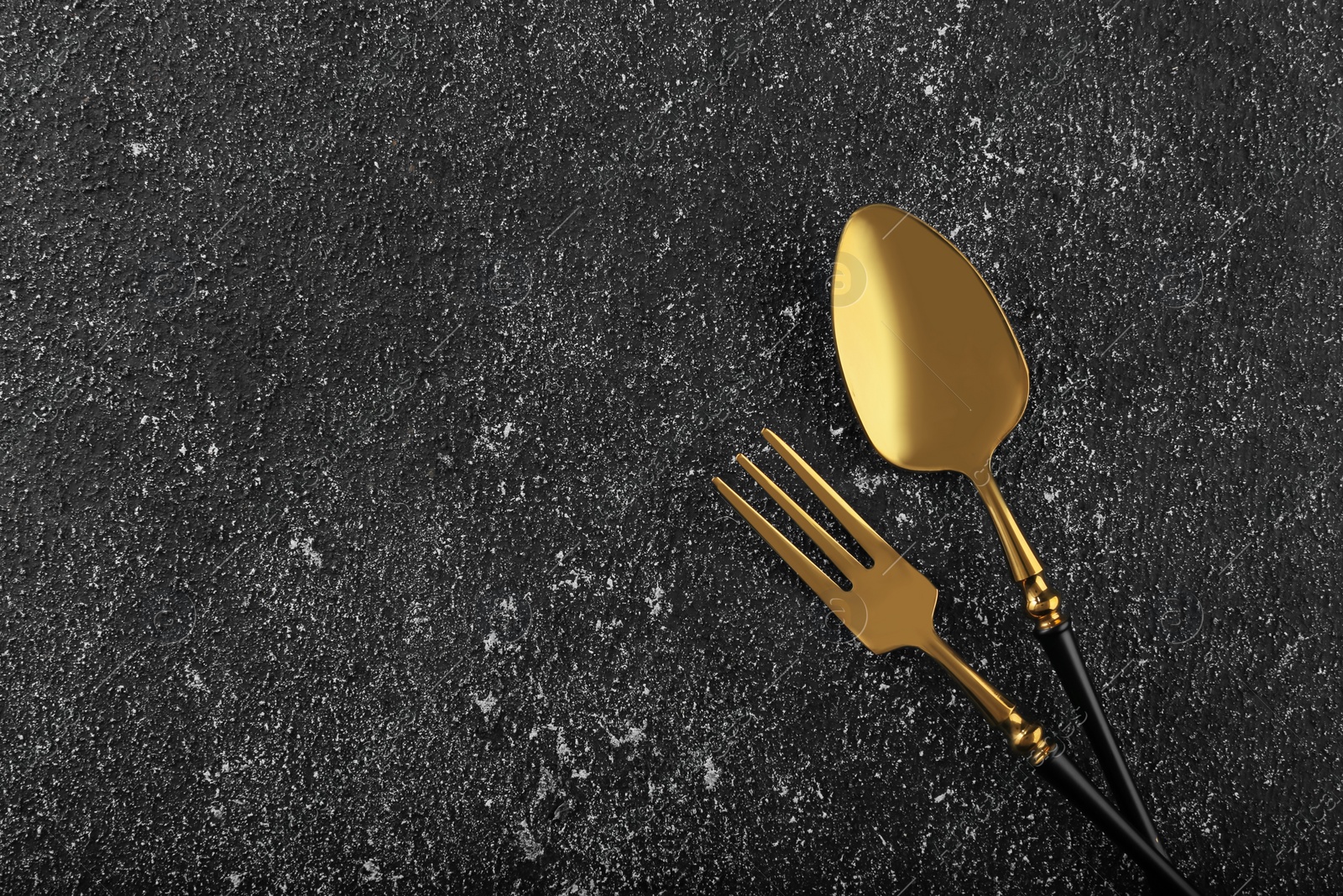 Photo of Shiny fork and spoon on black table, flat lay. Space for text