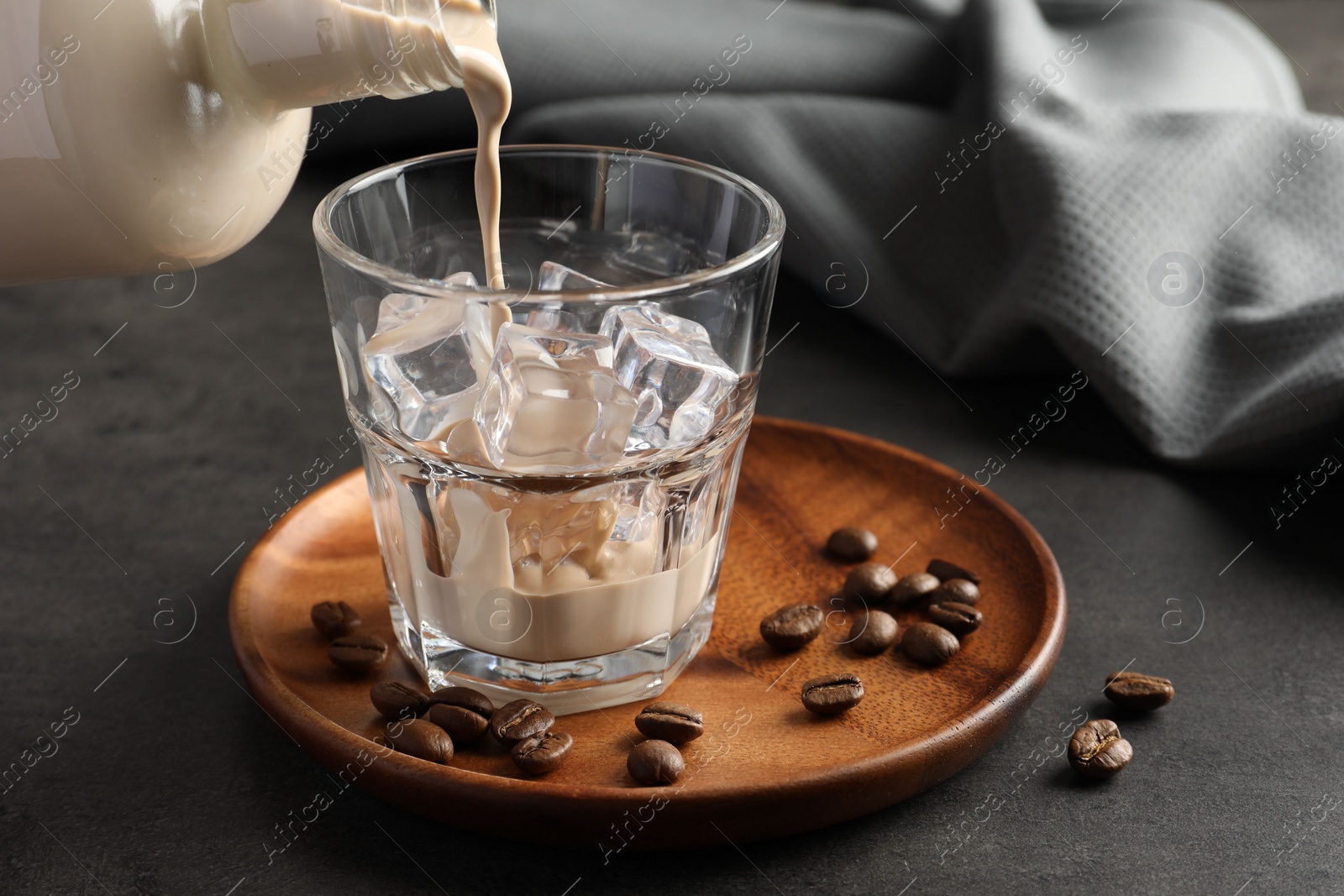 Photo of Pouring coffee cream liqueur into glass at grey table, closeup