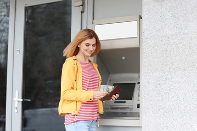 Beautiful woman with money near cash machine outdoors