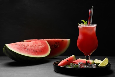 Tasty watermelon drink with mint on grey table against black background