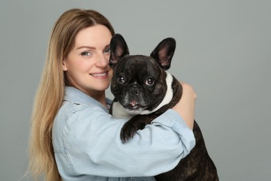 Photo of Portrait of happy woman hugging cute French Bulldog on grey background, space for text