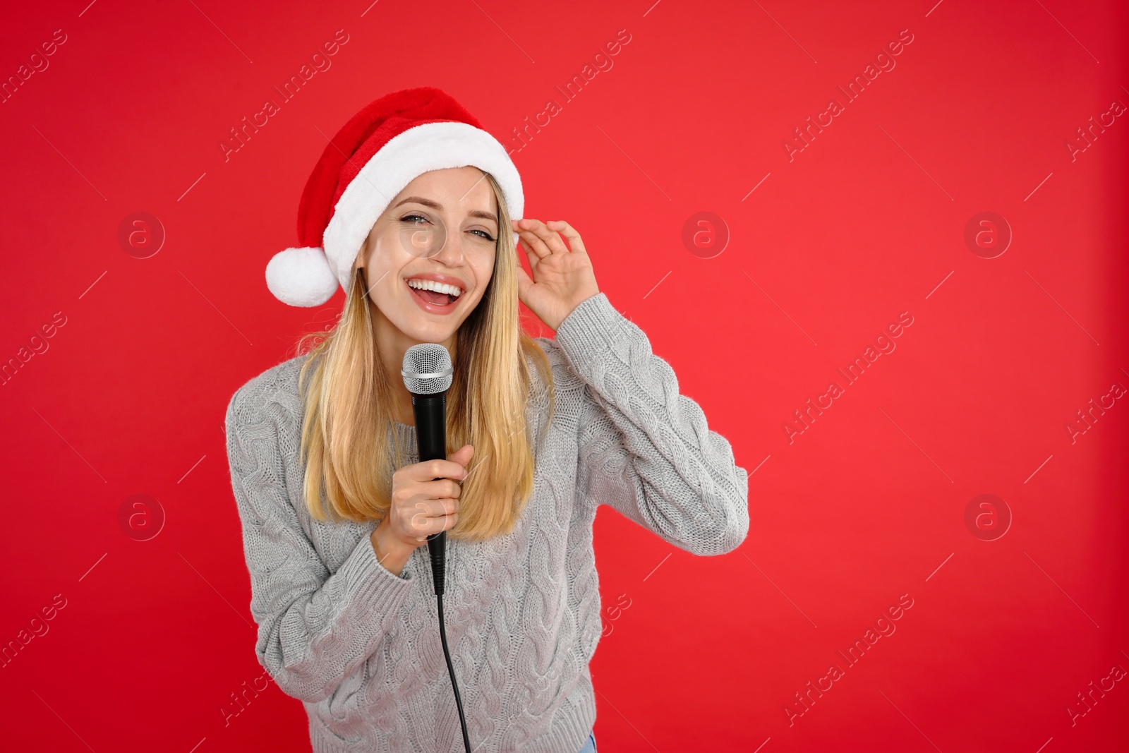 Photo of Emotional woman in Santa Claus hat singing with microphone on red background, space for text. Christmas music