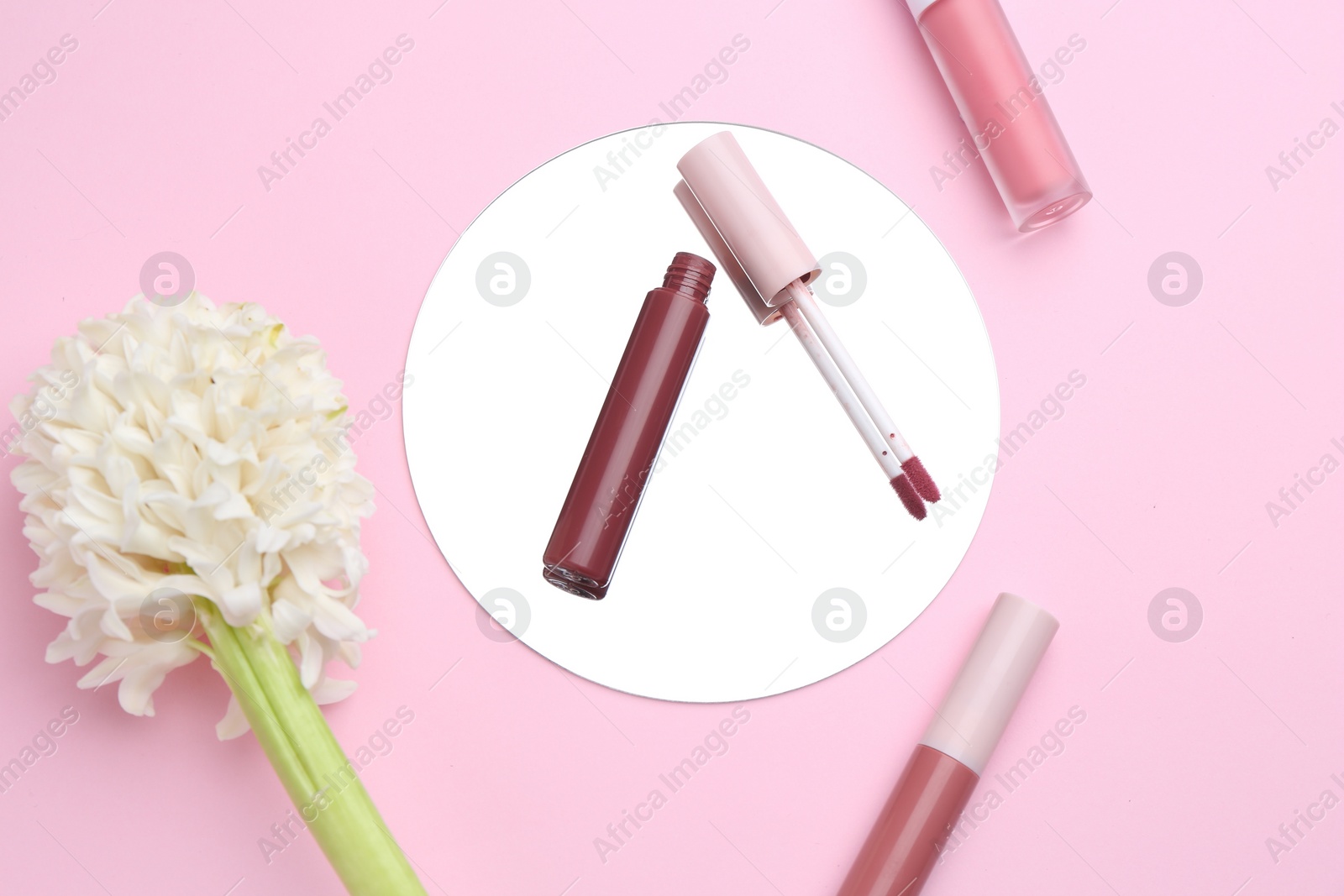 Photo of Different lip glosses, hyacinth and mirror on pink background, flat lay