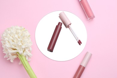 Photo of Different lip glosses, hyacinth and mirror on pink background, flat lay