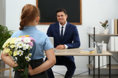 Photo of Schoolgirl with bouquet congratulating her pedagogue in classroom. Teacher's day