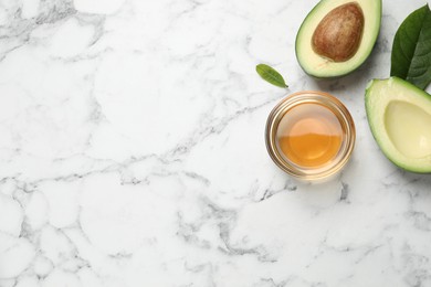 Flat lay composition with essential oil and avocado on white marble table. Space for text
