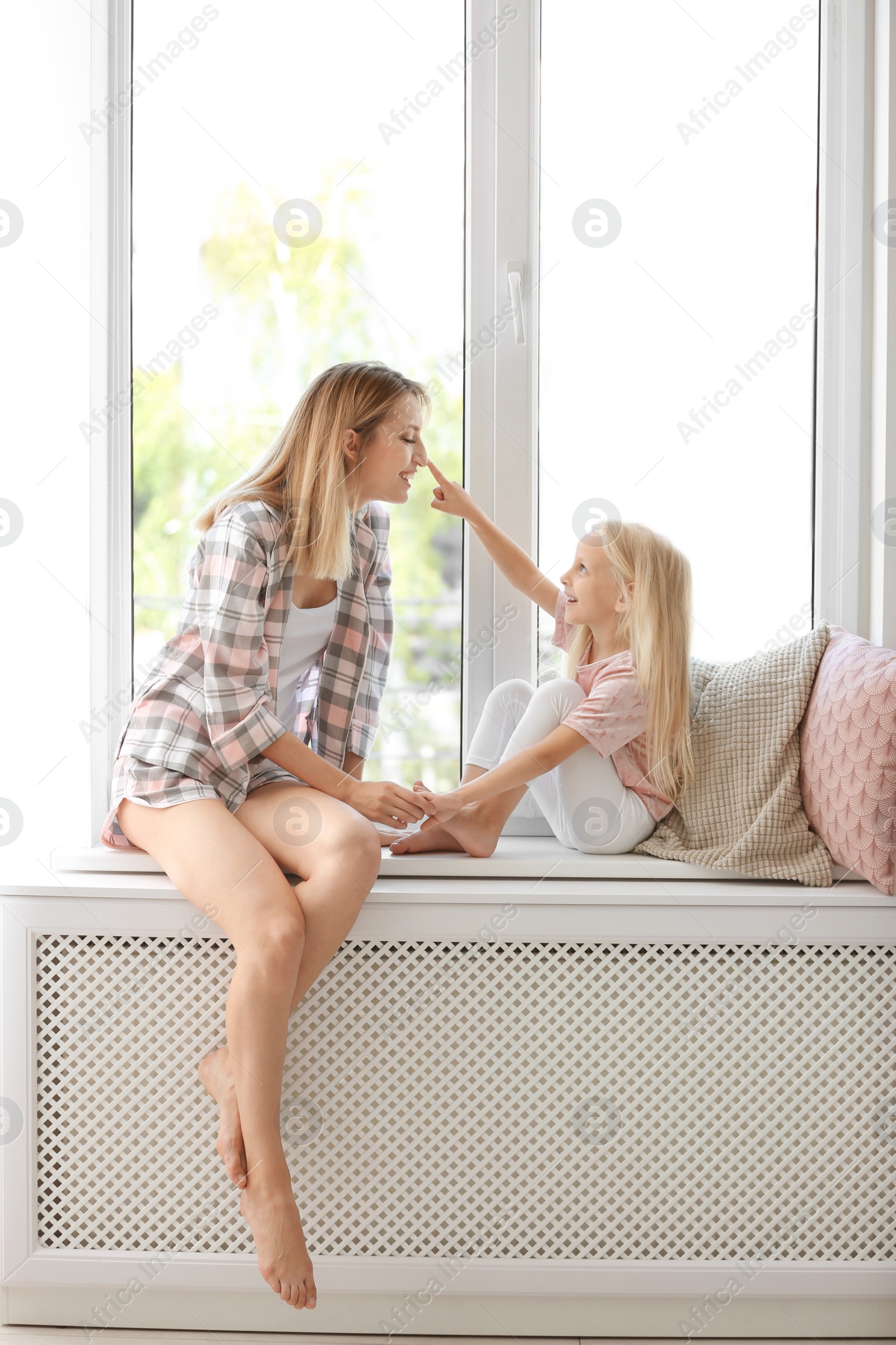 Photo of Young woman with cute little girl near window at home