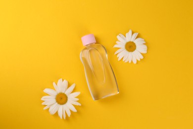 Bottle with baby oil and daisies on orange background, flat lay