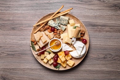 Cheese plate with honey, grapes and nuts on wooden table, top view