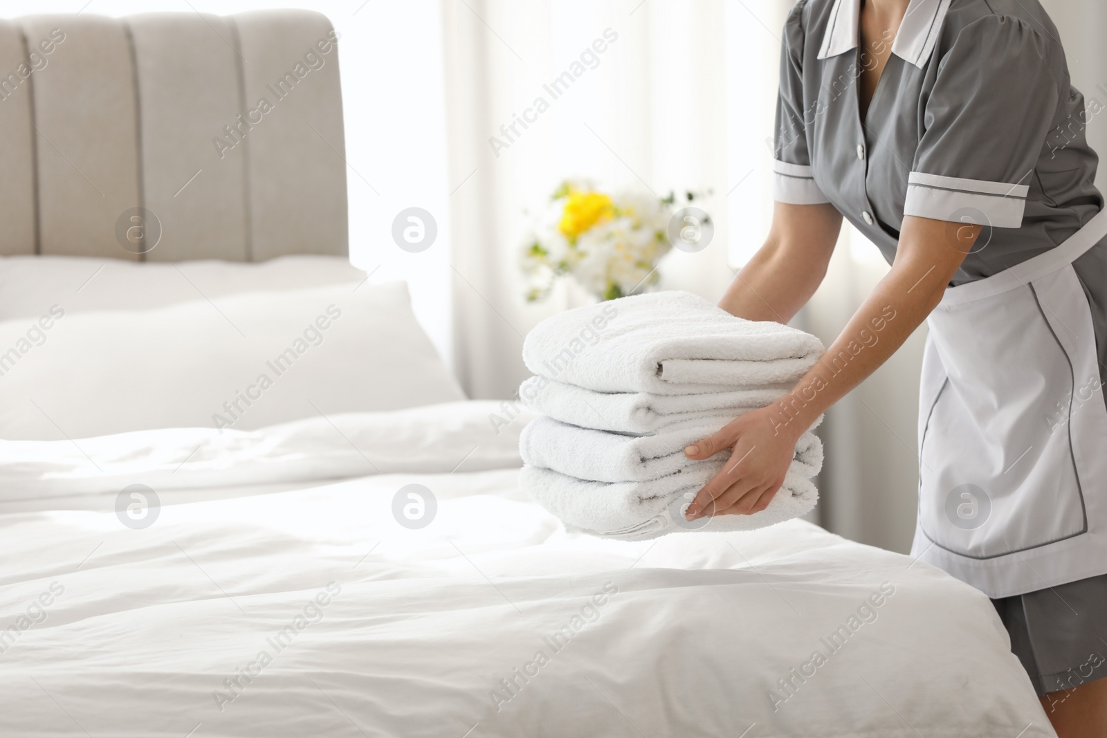 Photo of Young chambermaid putting stack of fresh towels in bedroom, closeup. Space for text