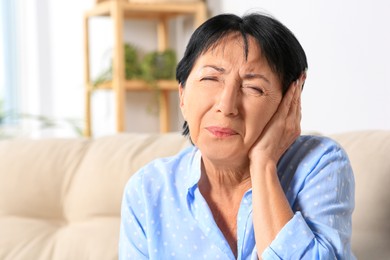 Photo of Senior woman suffering from ear pain at home. Space for text