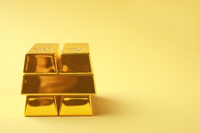 Stack of shiny gold bars on yellow background. Space for text