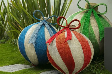 Photo of Beautiful shiny Christmas baubles on green grass outdoors. Festive street decorations