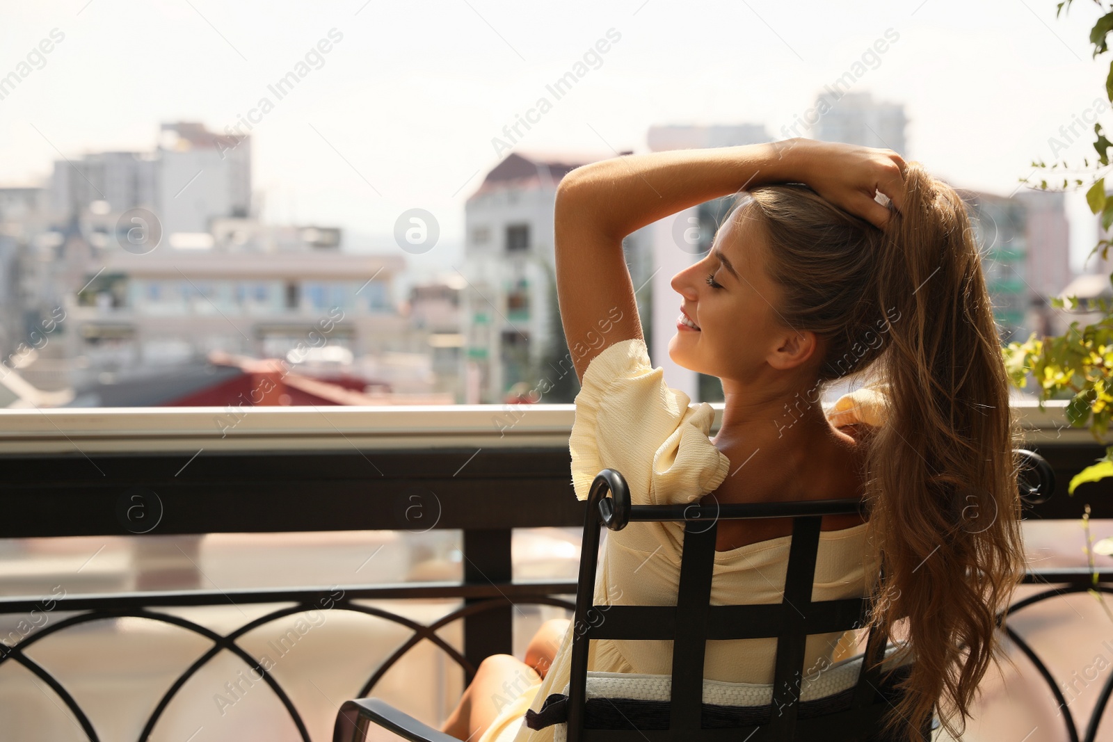 Photo of Beautiful young woman sitting on balcony, back view. Space for text