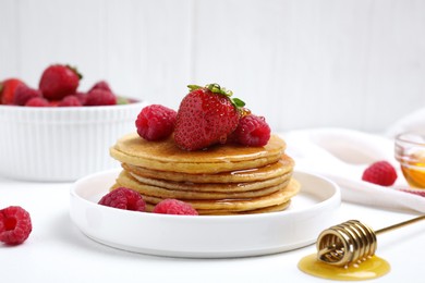 Tasty pancakes with fresh berries and honey on white table