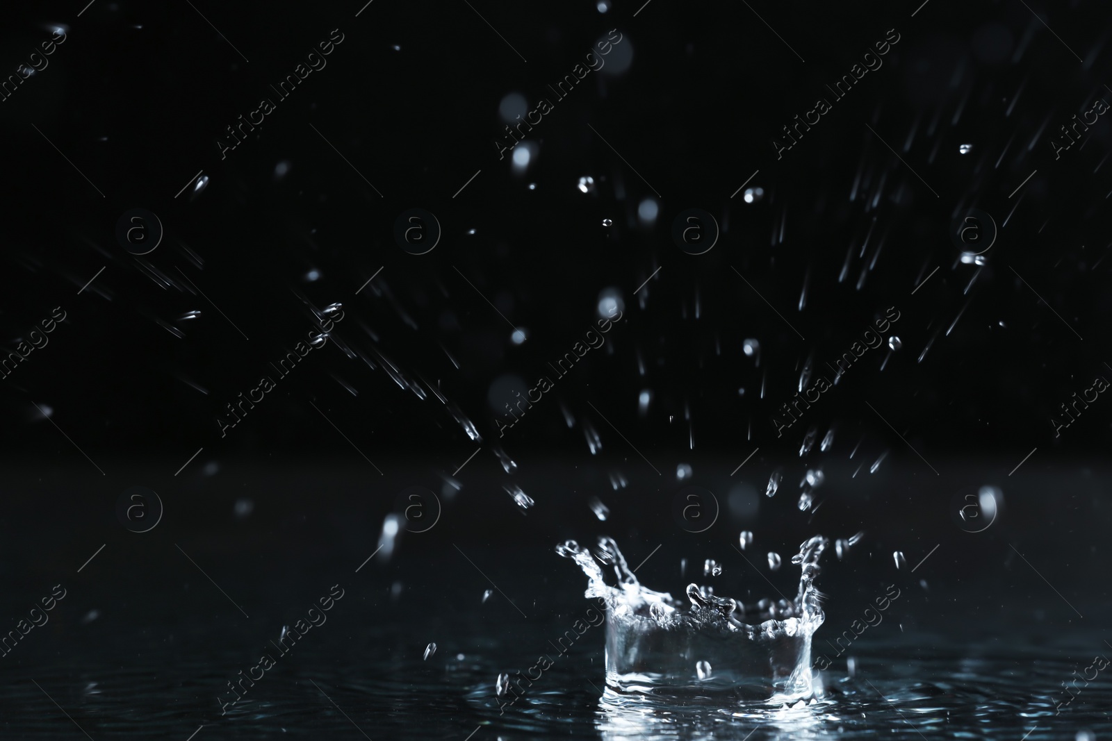 Photo of Rain drop falling down into puddle on dark background