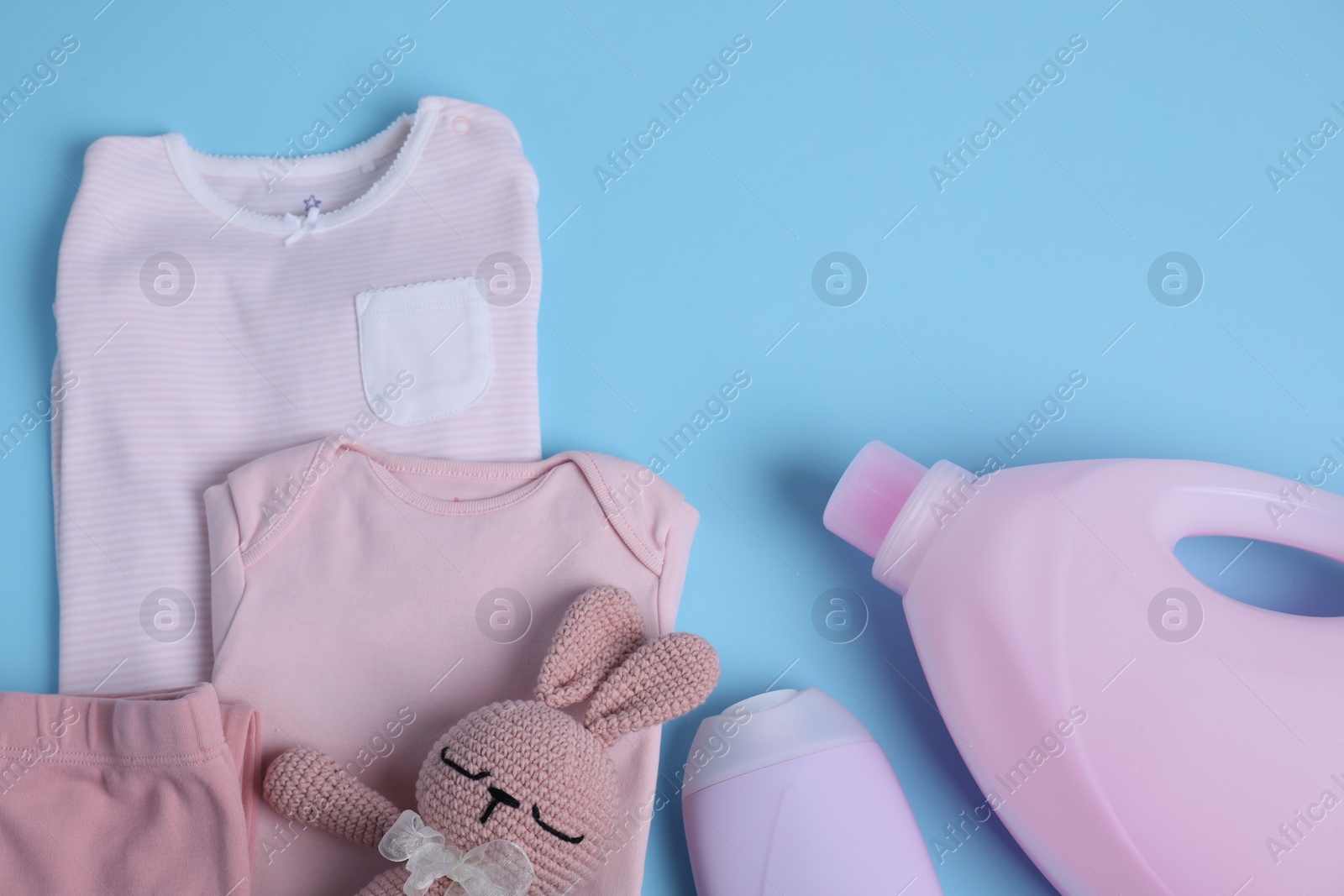 Photo of Bottles of laundry detergents, baby clothes and toy bear on light blue background, flat lay. Space for text