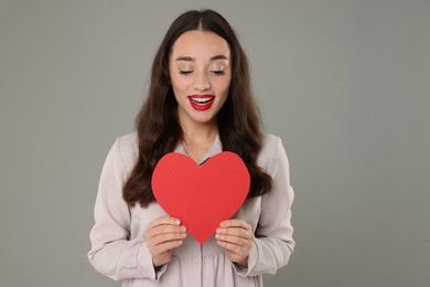 Beautiful young woman with paper heart on grey background