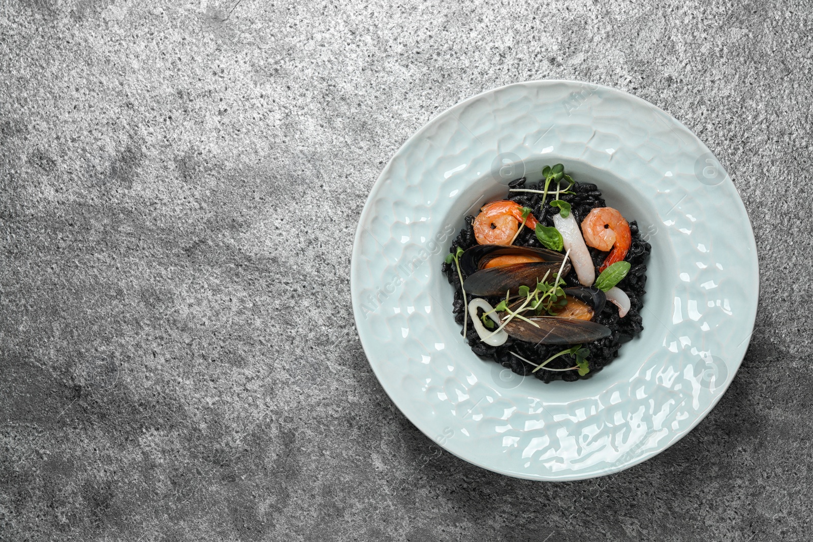 Photo of Delicious black risotto with seafood on grey table, top view. Space for text