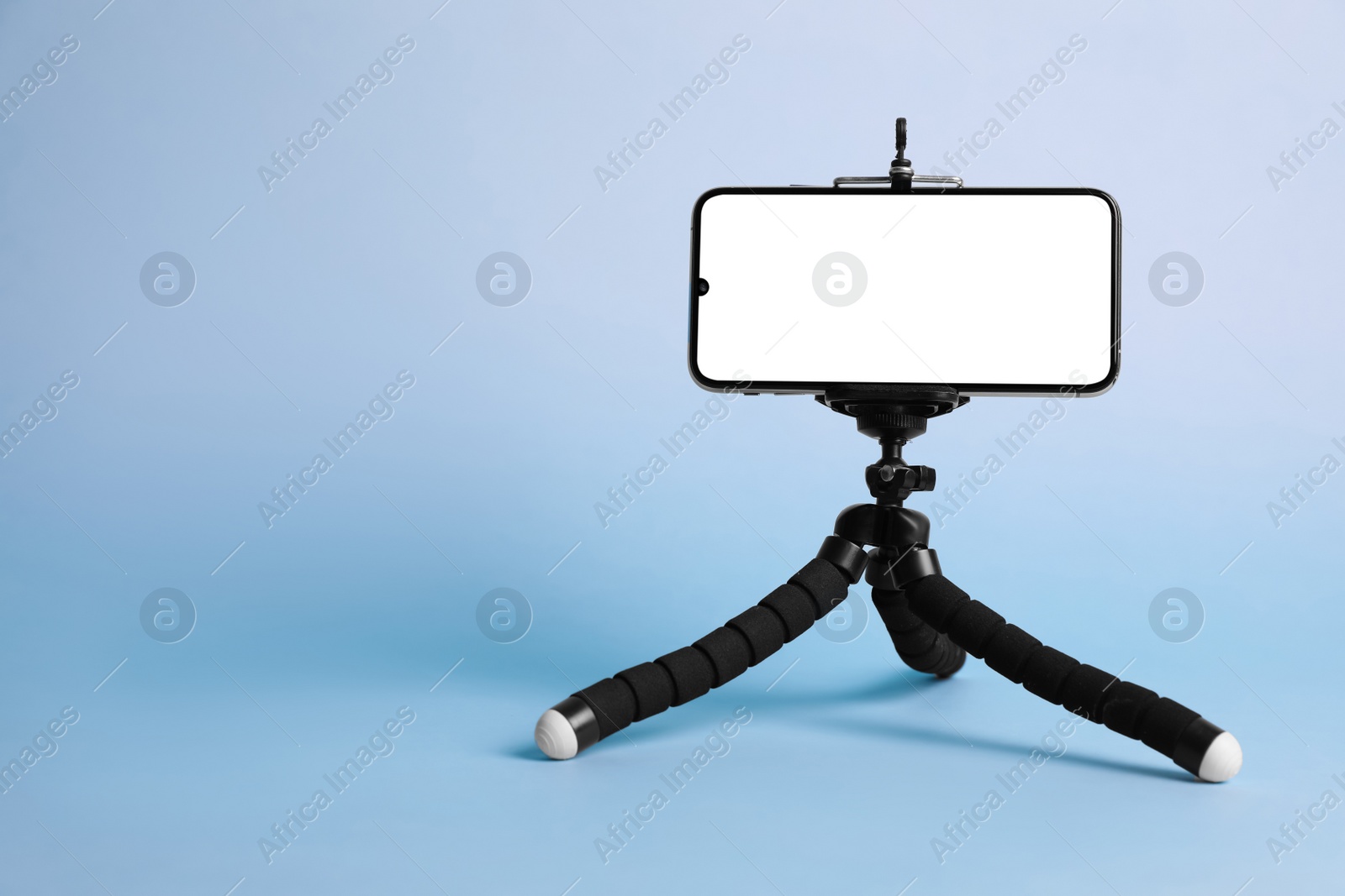 Photo of Modern tripod with smartphone on light blue background. Space for text