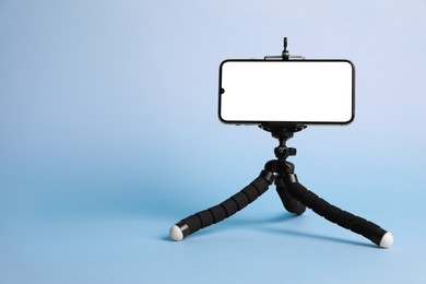 Modern tripod with smartphone on light blue background. Space for text