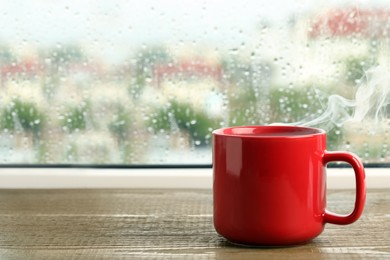 Photo of Cup of hot drink near window on rainy day. Space for text