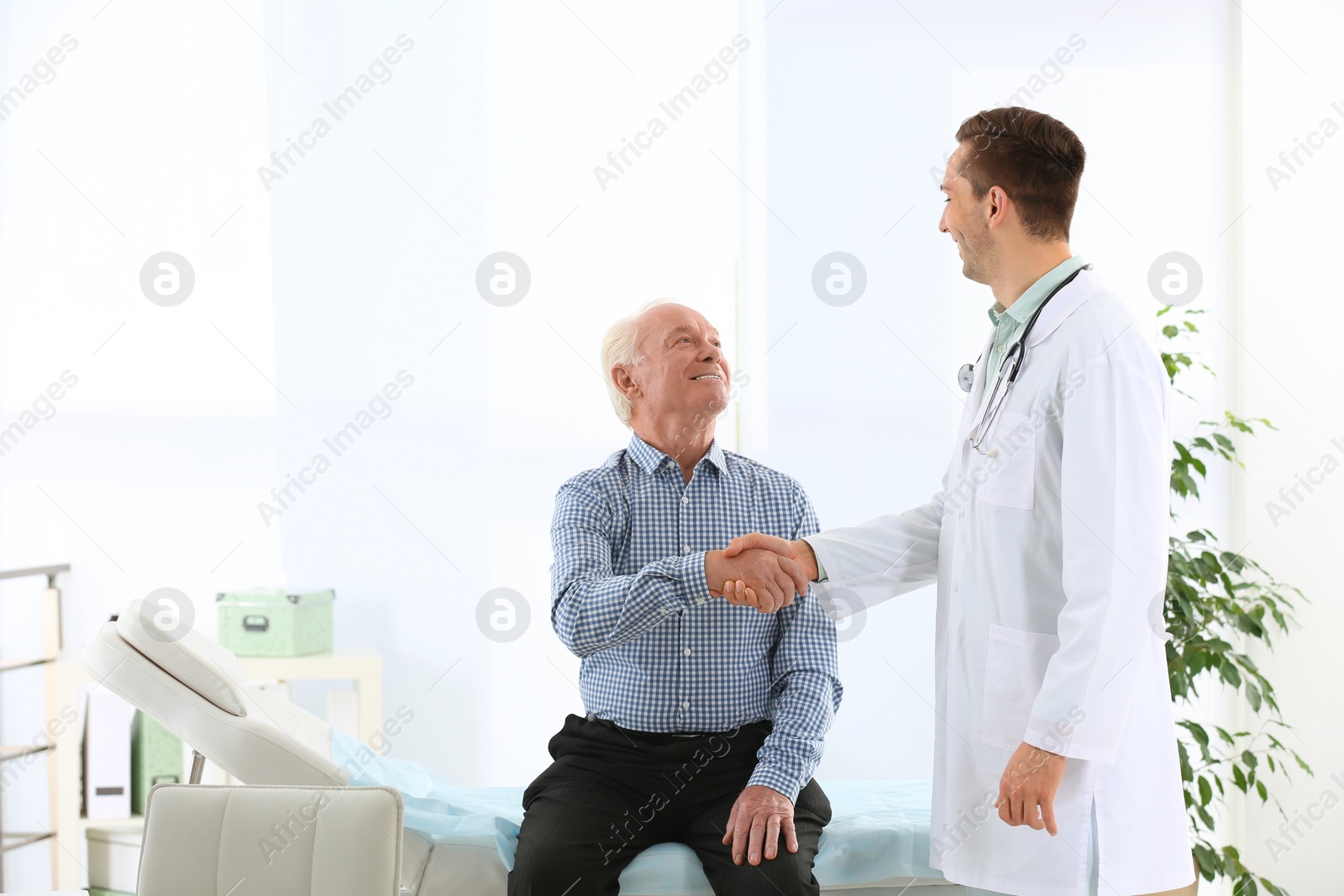 Photo of Doctor and elderly patient shaking hands in hospital. Space for text