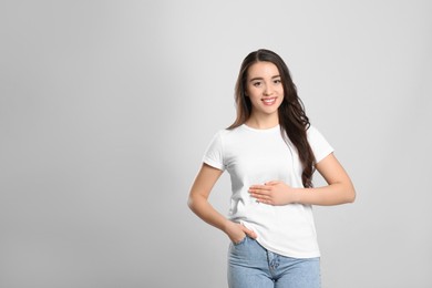 Photo of Happy healthy woman touching her belly on light grey background, space for text