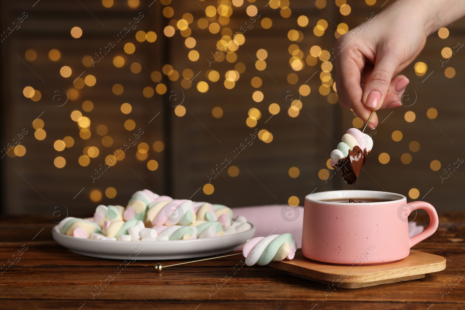 Photo of Woman dipping marshmallow into cup of delicious hot chocolate at wooden table, closeup