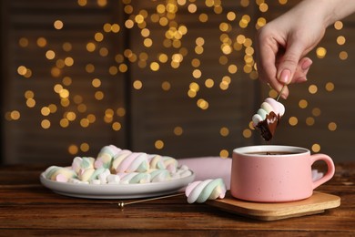 Woman dipping marshmallow into cup of delicious hot chocolate at wooden table, closeup
