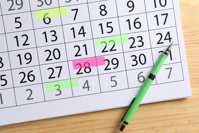 Timetable. Calendar page with marked dates and pen on wooden table, top view