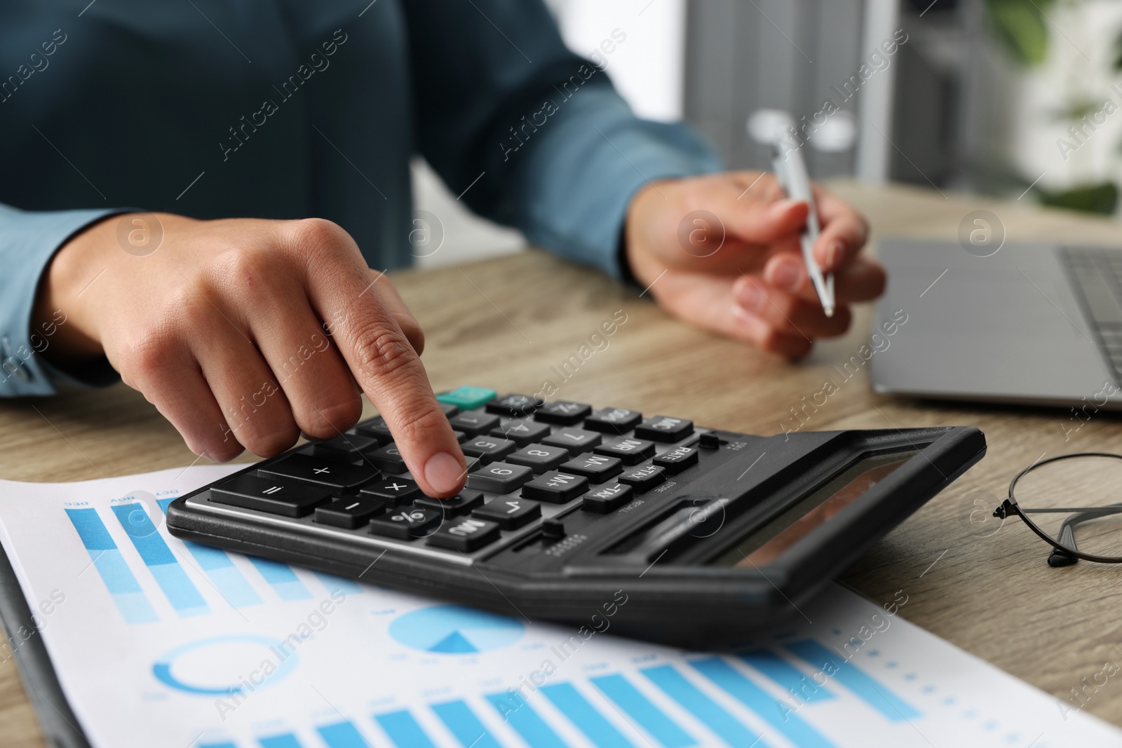 Photo of Woman using calculator at wooden table, closeup