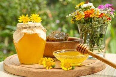 Delicious honey, combs and different flowers on wooden table in garden