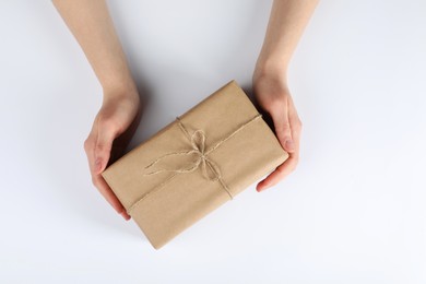 Woman holding parcel wrapped in kraft paper on white background, top view