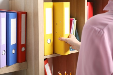 Woman taking binder office folder from shelving unit, closeup