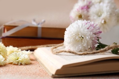 Book with chrysanthemum flowers as bookmark on beige textured table, closeup. Space for text