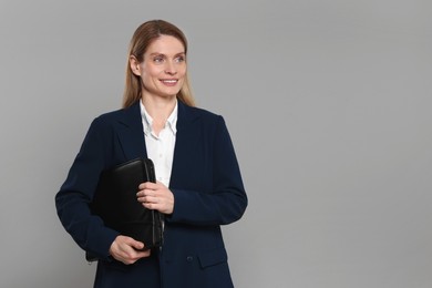 Photo of Happy real estate agent with leather portfolio on grey background. Space for text