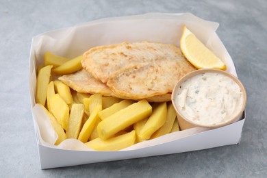 Photo of Delicious fish and chips with tasty sauce in paper box on gray table, closeup